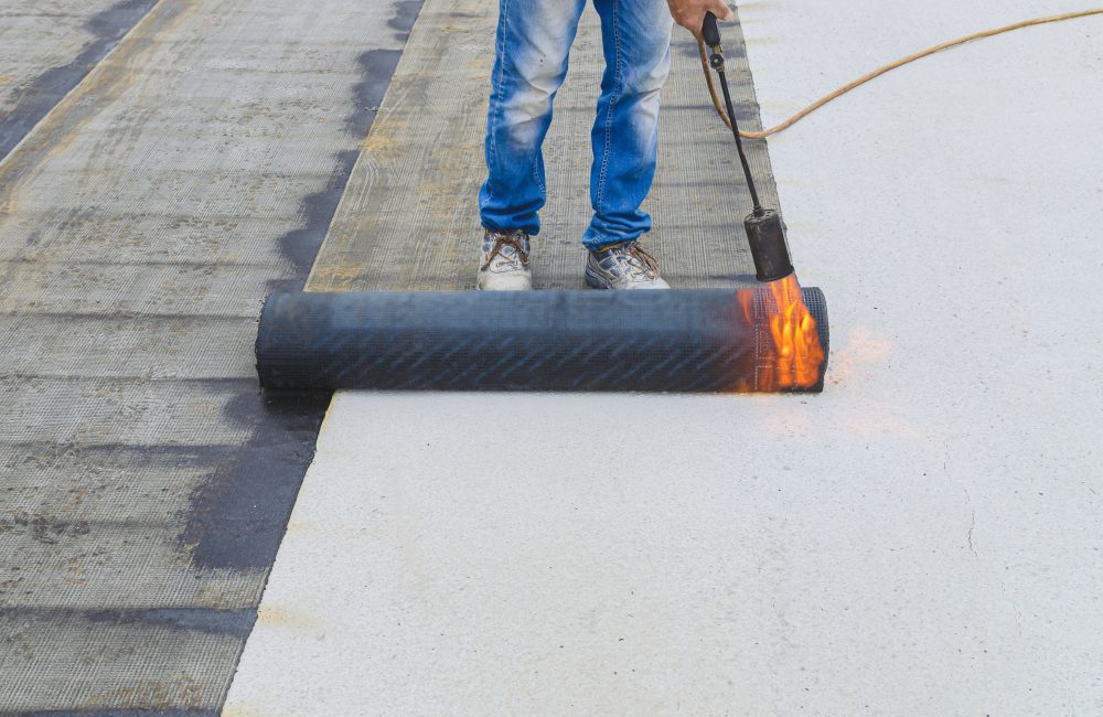 workers insulating rooftop with bitumen membrane. Waterproofing details at construction site. System details and installation on flat rooftop.